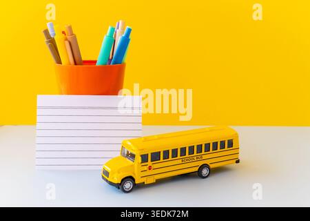 Bright minimal still life featuring toy school bus, blank lined card and colorful pens in a cup, capturing back to school core trend, dopamine Stock Photo