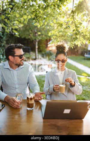 Coworkers having outdoor business meeting discussing projects on laptop Stock Photo