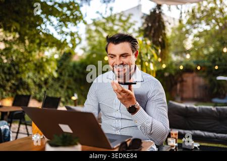 Man dictating voice message using phone outdoors with laptop Stock Photo