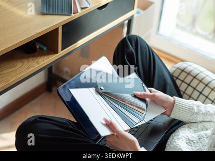 Woman holding material swatches while using laptop for creative home decorating Stock Photo