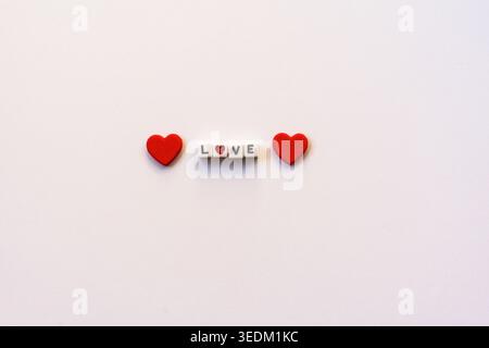 Minimal composition with red hearts and the word LOVE on clean white background, romantic concept with copy space. Stock Photo