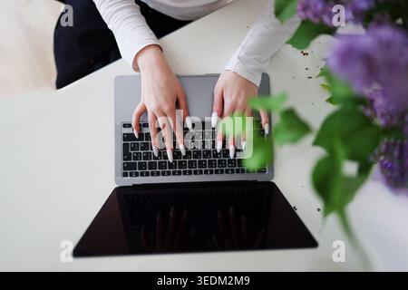 Minimalist workspace with woman using laptop and fresh lilac bouquet, combining productivity, spring mood and modern lifestyle. Stock Photo
