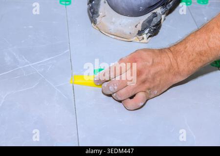 Contractor installs tiles on floor, using yellow spacers for even gaps spacing in construction area. Stock Photo