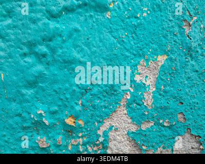 Close-up texture of a bumpy teal-painted wall with areas of flaking and peeling revealing grey concrete beneath. Stock Photo