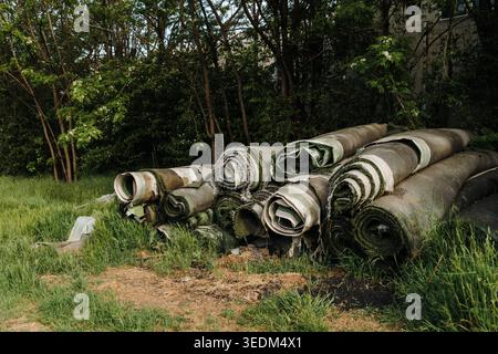 Pile of old rolled artificial grass stored outdoors near trees and overgrown vegetation. Waste management, recycling, landscaping, renovation, and Stock Photo