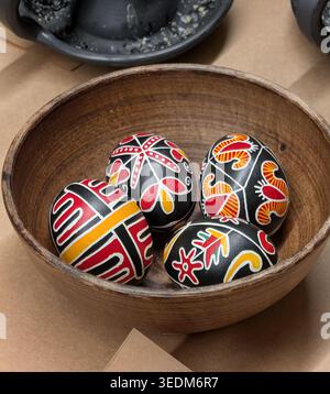 Four traditional Ukrainian Pysanky Easter eggs with geometric & floral patterns in rustic wooden bowl. Top-down view of hand-painted Ukrainian Pysanky Stock Photo