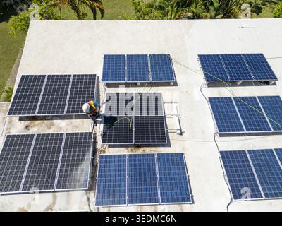 Aerial view of a worker in a safety vest cleaning solar panels on a flat roof surrounded by tropical greenery in Guanaja, Bay Islands Department, Hond Stock Photo