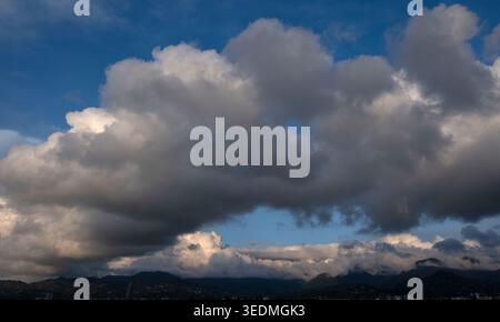 Large white cumulus clouds over a coastal city and mountains Stock Photo