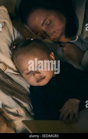 Cute girl sleeping with mother on bed at home Stock Photo