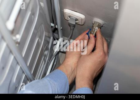 A worker installing or repairing a plumbing valve, likely for a washing machine Stock Photo