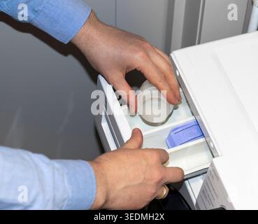 Man adding washing detergent to the detergent dispenser drawer of a front-load washing machine Stock Photo