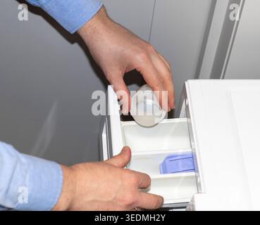 Man adding washing detergent to the detergent dispenser drawer of a front-load washing machine Stock Photo