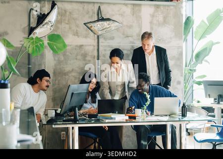 Investors communicating with team of employees working on laptop at office Stock Photo