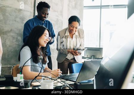 Group of business professionals smiling while looking at laptop screen in modern office Stock Photo