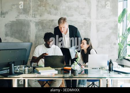 Male investor discussing business ideas with employees sitting at desk in startup workspace Stock Photo