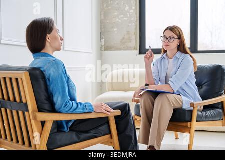 Psychologist with glasses taking notes during counseling session with young female client Stock Photo