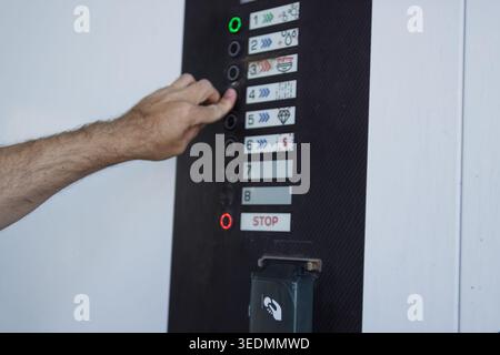 Hand pressing button on a self-service car wash control panel to start a wash program, selecting cleaning options on a modern outdoor machine interfac Stock Photo