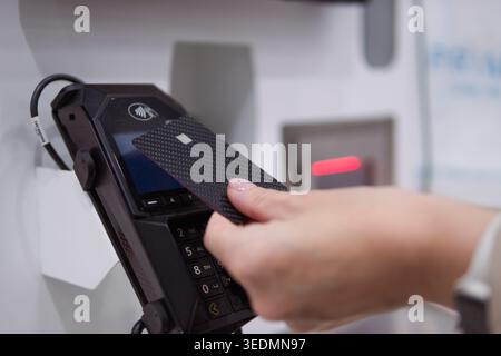 Woman's hand tapping a credit card on a pos terminal for a fast, secure contactless payment, close-up indoor shot emphasizing modern digital finance a Stock Photo