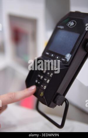 Customer finger pressing buttons on a payment terminal keypad, securely entering pin code for credit or debit card transaction during a retail purchas Stock Photo