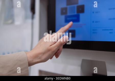 Hand with a manicured finger is touching a blue button on a digital touchscreen, interacting with the graphical user interface of a modern self-servic Stock Photo