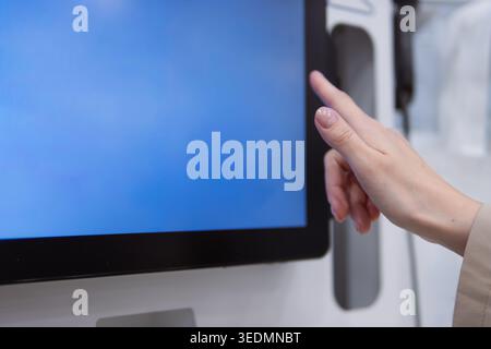 Woman's hand interacting with a self-service interactive kiosk touchscreen interface, using finger to make a selection on the blue monitor for modern Stock Photo