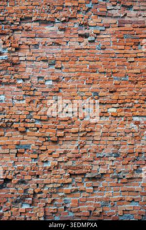 Ancient damaged clay brick wall texture with rough masonry as architectural background . Old rustic orange brickwork surface in portrait orientation f Stock Photo