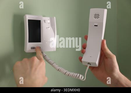 Man with handset pressing button on intercom panel indoors, closeup Stock Photo