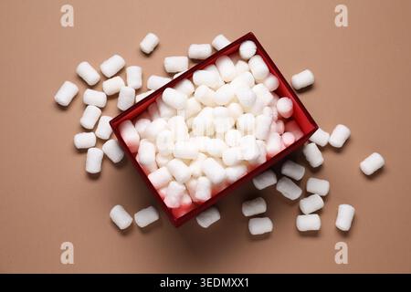Gift box with packing peanuts on brown background, flat lay Stock Photo