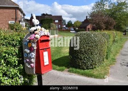 Royal Mail Red post box with Knitted Toppers for easter decoration in the village of Oxton Nottinghamshire,UK. Stock Photo