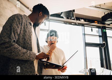 Male computer programmers discussing ideas while working on laptop at modern startup office Stock Photo