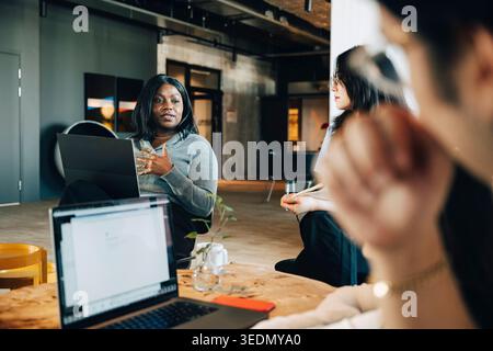 Businesswoman communicating with team while sitting at startup workspace Stock Photo
