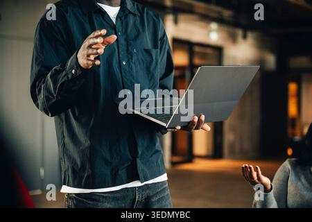 Midsection of male entrepreneur holding laptop and giving presentation to team at office Stock Photo