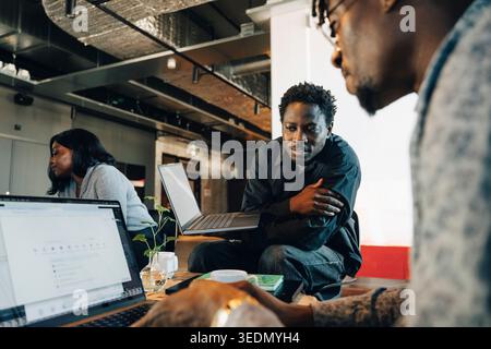 Male entrepreneurs discussing with each other while working on laptop at office Stock Photo
