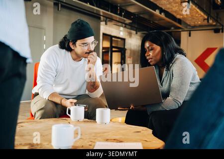Businesswoman sharing business idea with male colleague over laptop while sitting at startup workspace Stock Photo