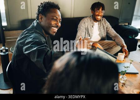 Happy male entrepreneur interacting with coworkers while discussing ideas at office Stock Photo