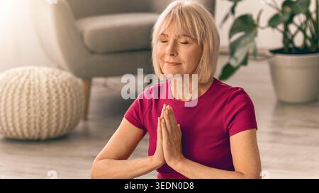 Older Woman Practices Yoga in Living Room During Morning Light With Plants Nearby Stock Photo