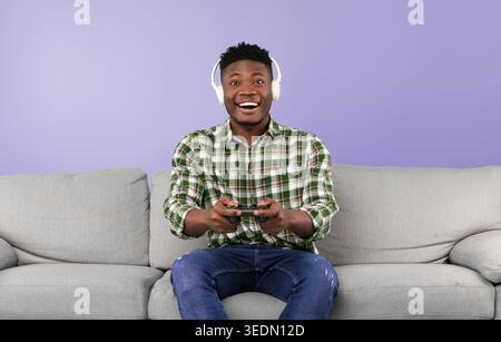 Man Enjoys Gaming at Home With Headphones and Smiles While Sitting on a Couch Stock Photo