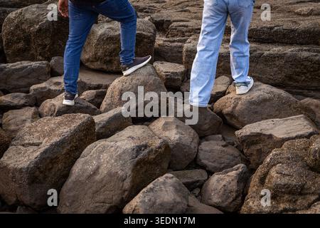 People Walking Across Rocky Seashore Boulders Outdoors Stock Photo