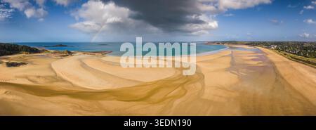 Aerial view of the expansive sandy beach and turquoise waters under a dramatic sky with a rainbow Plurien, Brittany, France. Stock Photo