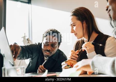 Diverse coworkers discussing business strategy while sitting at desk in modern startup office Stock Photo