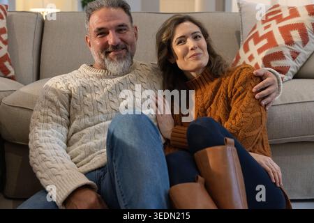 Couple sitting on floor in living room, leaning against sofa, wearing knit sweaters and boots Stock Photo