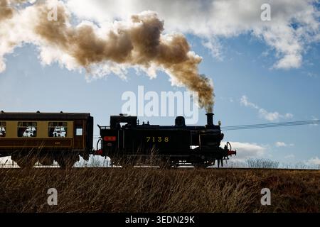 A steam train on a heritage railway silhouetted by bright sunshine with the smoke billowing from the funnel, East Lancashire Railway, Bury. Stock Photo