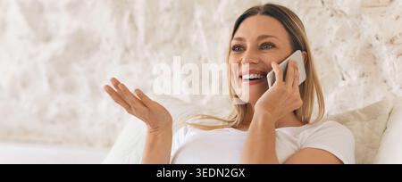 Smiling Woman Talking on the Phone While Sitting Indoors in a Light Environment Stock Photo