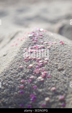 Pink glitter trail across dark beach sand texture Stock Photo