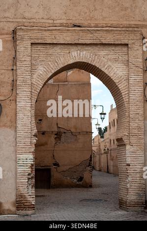 Sunlit archway in the Marrakech medina frames a narrow cobbled street with weathered mud-brick walls, traditional lanterns and a sense of history, dec Stock Photo