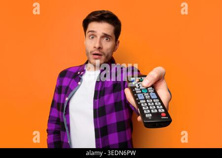 Man Holds Remote Control in a Studio With Orange Background During Evening Time Stock Photo