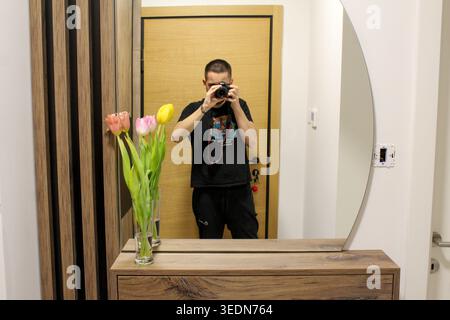 Man taking a photo in a mirror with tulips and wooden console in a modern hallway interior. Stock Photo