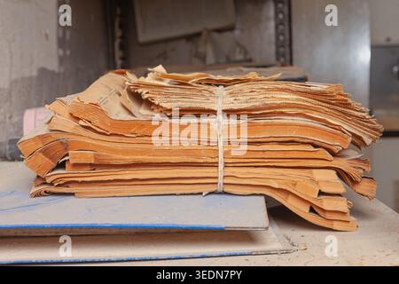A side-view of several deteriorated ledger books stacked on top of a blue arch lever file on a metal shelf. The visual texture shows compressed, warpe Stock Photo