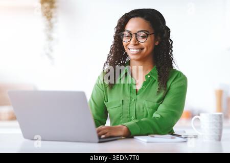 Young Woman Works on Laptop in Bright Workspace With Coffee Cup Nearby Stock Photo