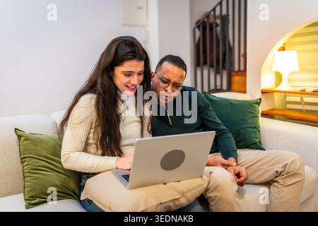 Interracial couple relaxing on sofa using laptop together Stock Photo